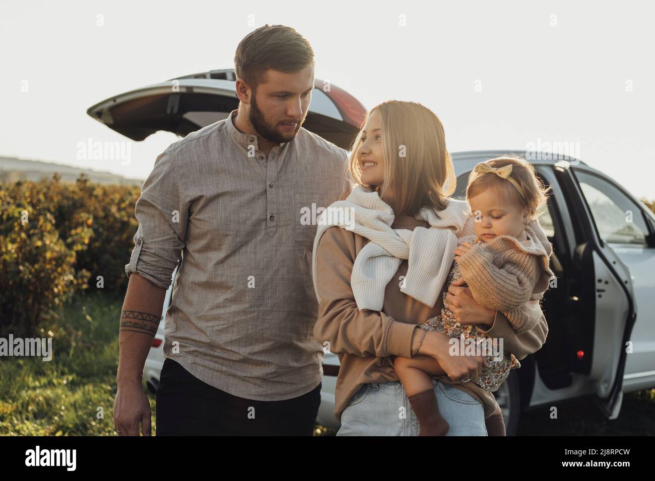 Giovane famiglia caucasica che si diverta su strada, madre e padre con bambina all'aperto con auto SUV sullo sfondo Foto Stock