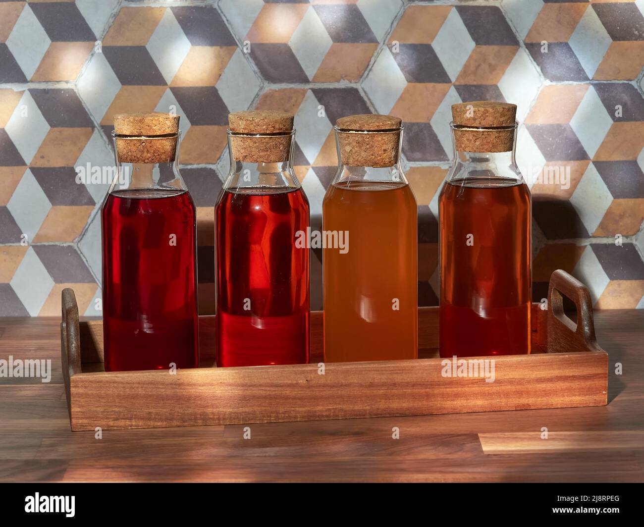Quattro bottiglie di tè freddo alla frutta, rooibos, verde e nero, in un vassoio di legno su un tavolo di legno Foto Stock