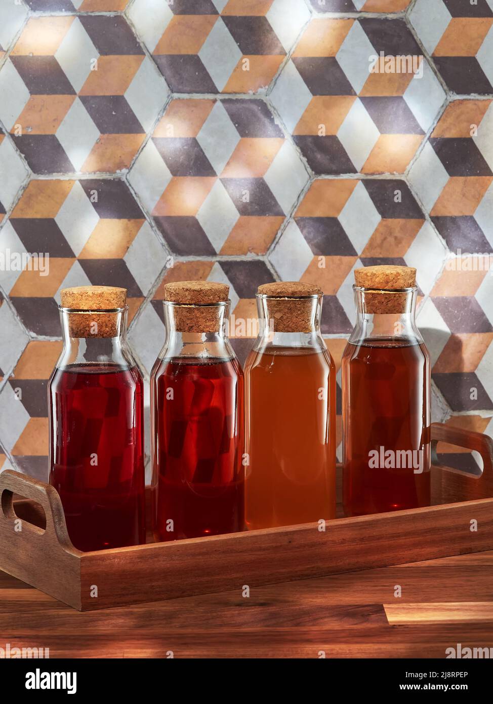 Quattro bottiglie di tè freddo alla frutta, rooibos, verde e nero, in un vassoio di legno su un tavolo di legno Foto Stock