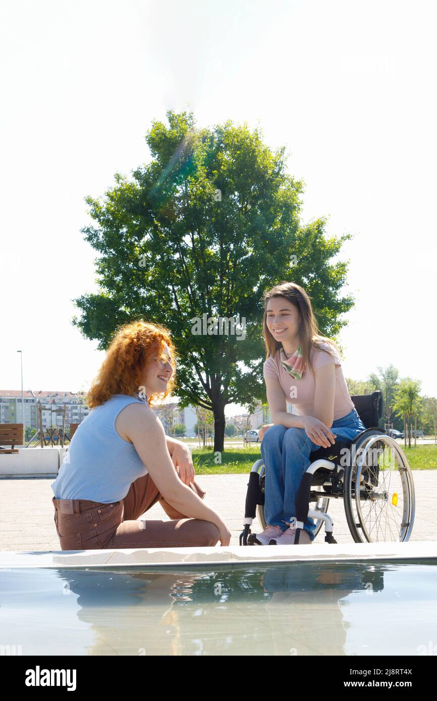 Due diversi amici che si divertono una giornata fuori con un albero nella parte posteriore che simboleggia la crescita della loro amicizia Foto Stock