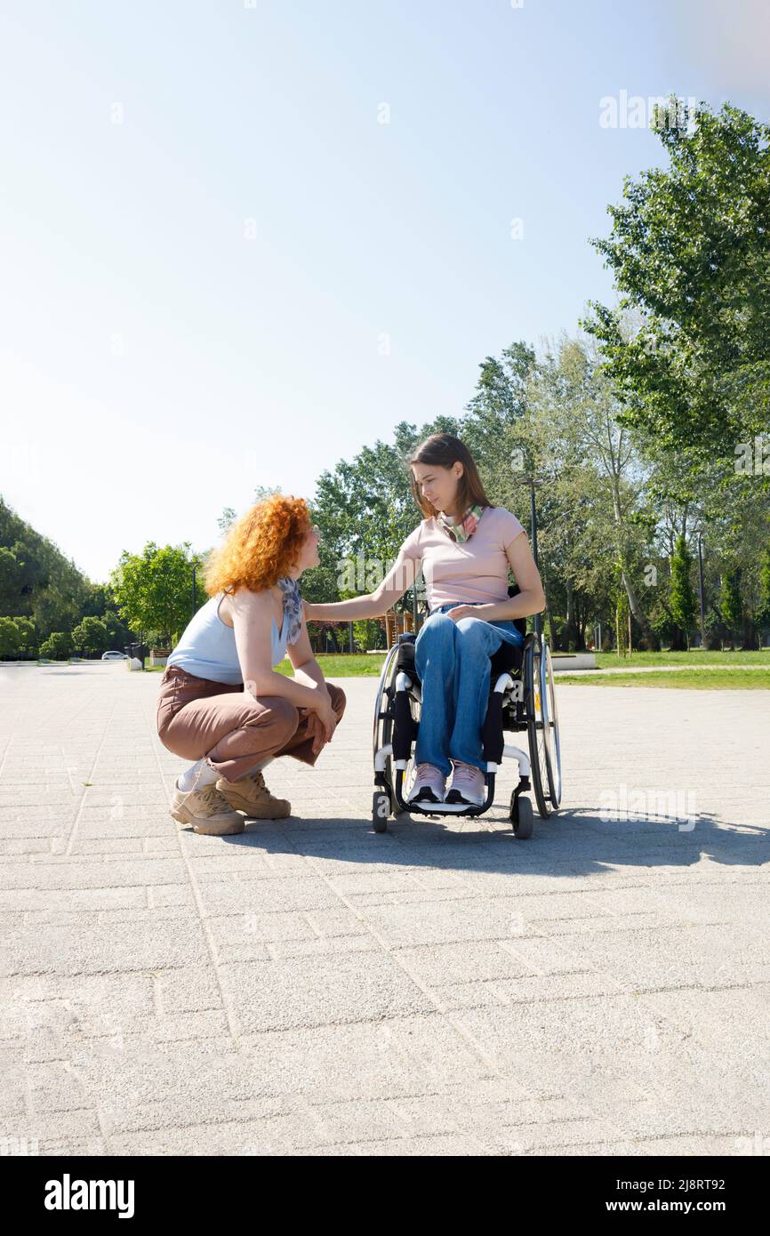 Donna disabile in sedia a rotelle che dà un consiglio alla sua amica femminile Foto Stock