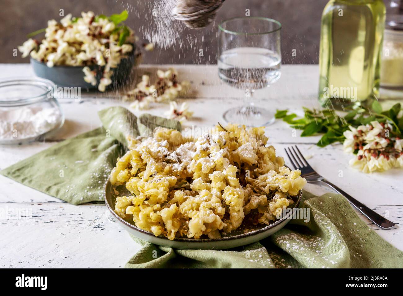 Fiori fritti di acacia o patatine fritte con olio, farina, acqua, zucchero in polvere sta cadendo a piatto. Messa a fuoco selettiva Foto Stock