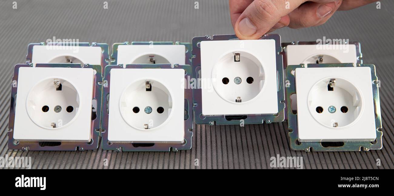 La mano di un uomo mette una presa elettrica in fila. Il concetto di installazione di dispositivi elettrici. Tariffe e risparmio energetico Foto Stock