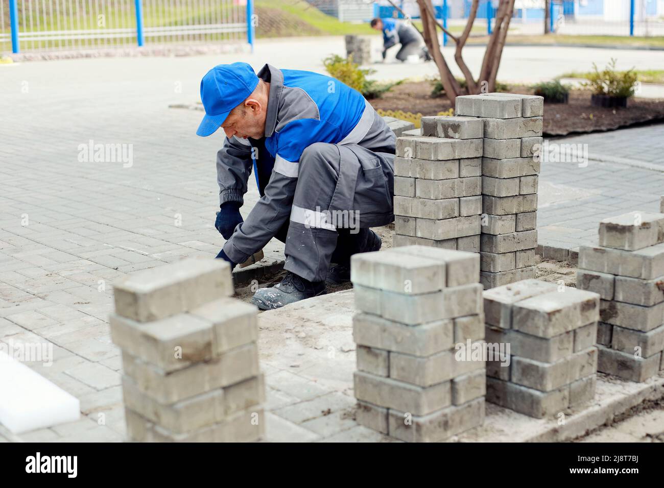 Il muratore stende le lastre di pavimentazione all'esterno. L'uomo che lavora esegue l'architettura paesaggistica. Il costruttore dispone il marciapiede con blocchi di pietra. Flusso di lavoro autentico. Duro lavoro in vecchiaia. Foto Stock