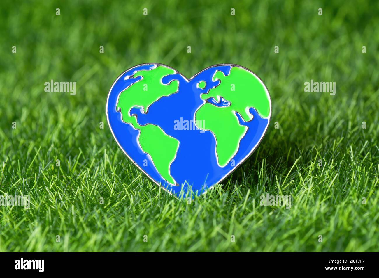 Primo piano di un perno a forma di cuore a forma di globo su sfondo verde di erba. Concetto ecologico di vita e cura della natura. Foto Stock