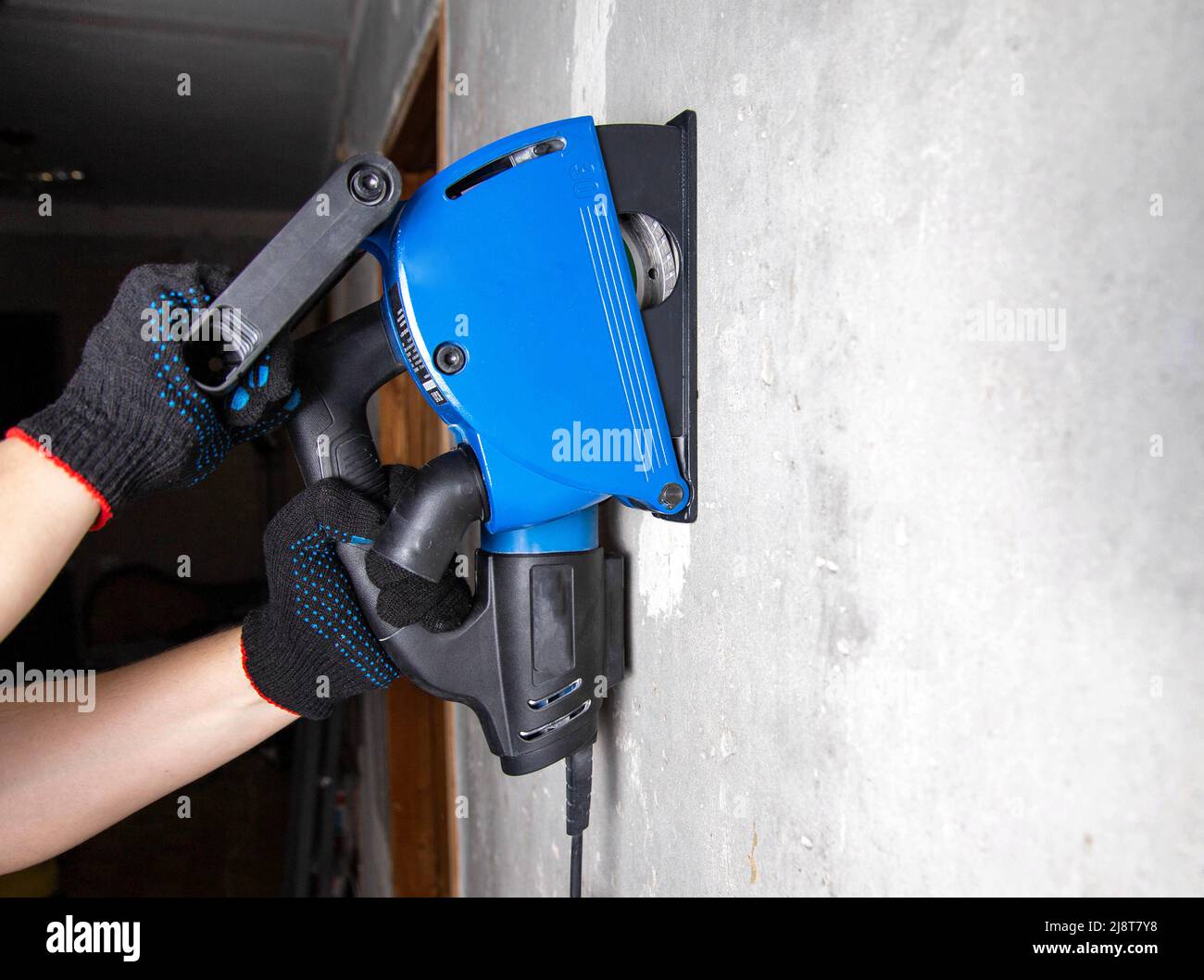 Un operatore in guanti lavora con un utensile elettrico con uno smaschiatore da parete su una parete di cemento armato. Foto Stock