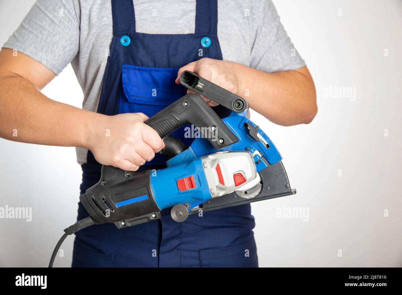 Un elettricista in tute tiene in mano uno smaschiatore per la realizzazione di cancelli nelle pareti. Foto Stock