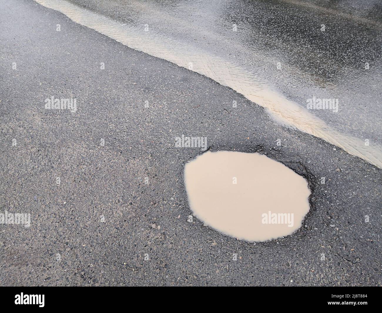 Buco e pozzanghere su strada rotta male. Distrutta strada con Puddle. Strada sbagliata. Pozzanghere e sporcizia su strada sterrata. Foto Stock