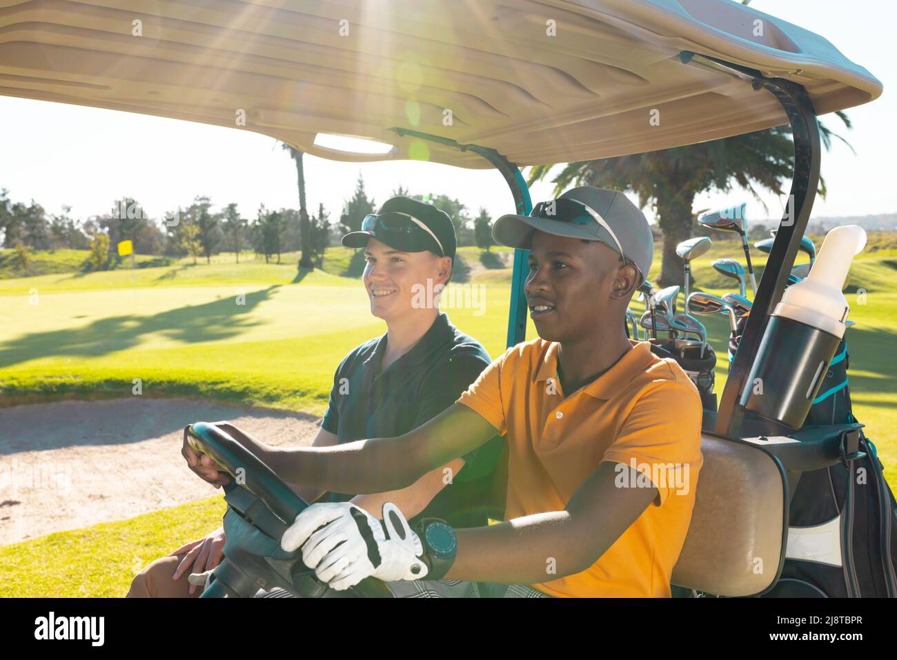 Giovane americano africano con amico maschio caucasico seduto in golf cart al campo di golf in estate Foto Stock
