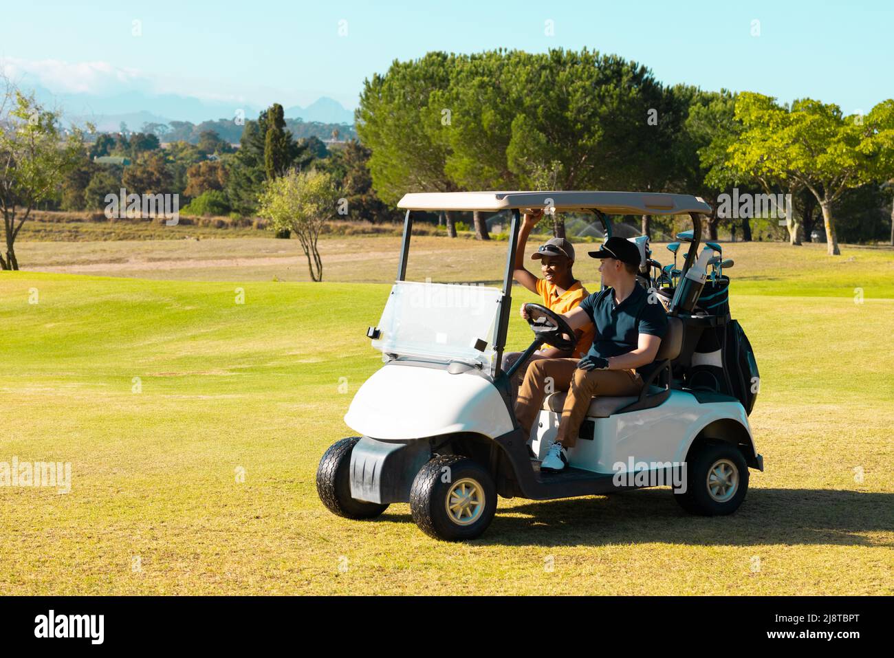 Amici maschi giovani multirazziali che parlano mentre si siede in golf cart nel campo di golf durante la giornata di sole Foto Stock