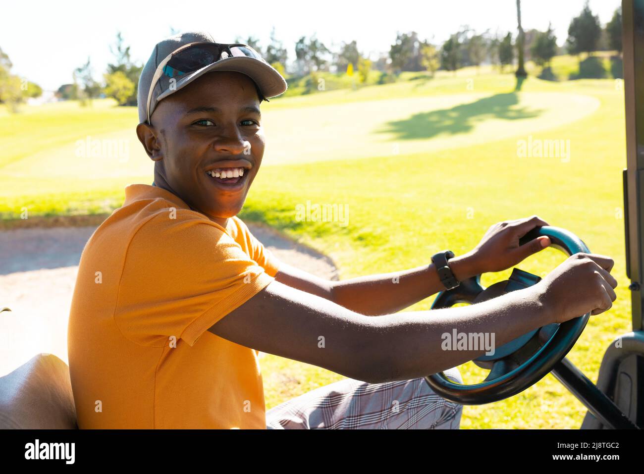 Ritratto di felice afroamericano giovane uomo che indossa cappello guida golf cart al campo da golf Foto Stock