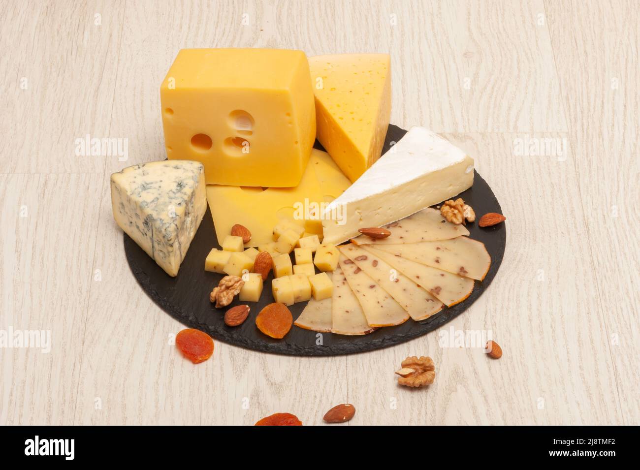 Diversi tipi di formaggio su un cartone di grafite con noci e frutta secca Foto Stock