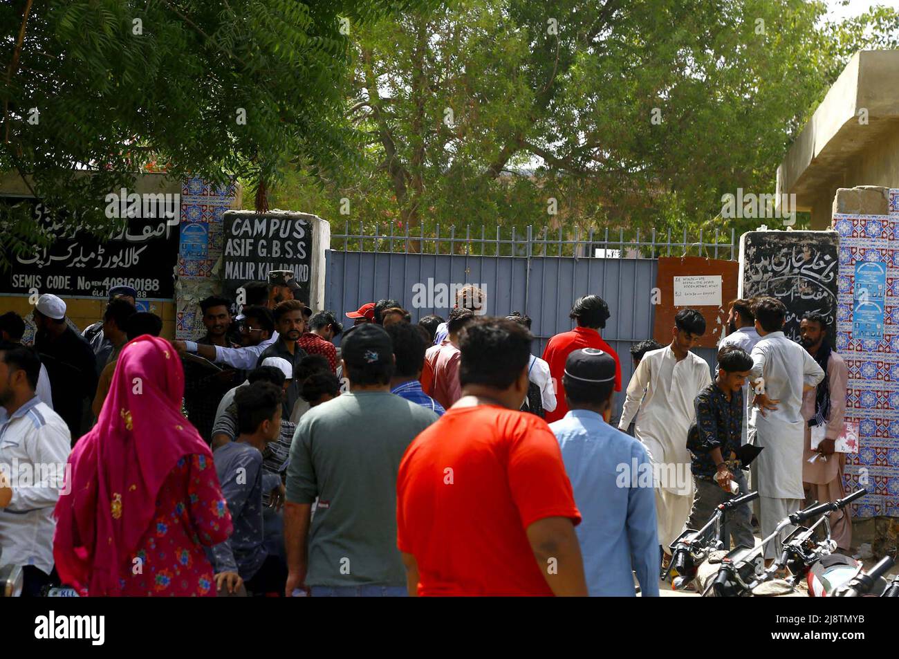 I genitori e gli studenti si riuniscono fuori dal centro di esame in una calda giornata estiva durante l'esame annuale di Matriculation 2022 sotto la supervisione del Consiglio di Istruzione secondaria e secondaria superiore, situato nell'area del Consiglio di Amministrazione di Malir Kala a Karachi mercoledì 18 maggio 2022. Foto Stock