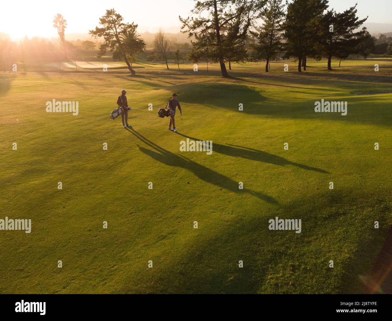 Vista aerea di giovani amici maschi multirazziali con borse a piedi sul campo da golf durante il tramonto Foto Stock