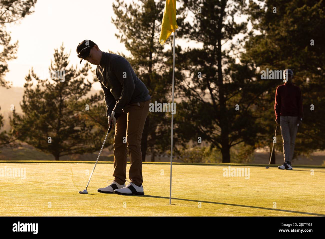 Giovane caucasico che gioca a golf con un giovane amico africano americano al campo di golf al tramonto Foto Stock