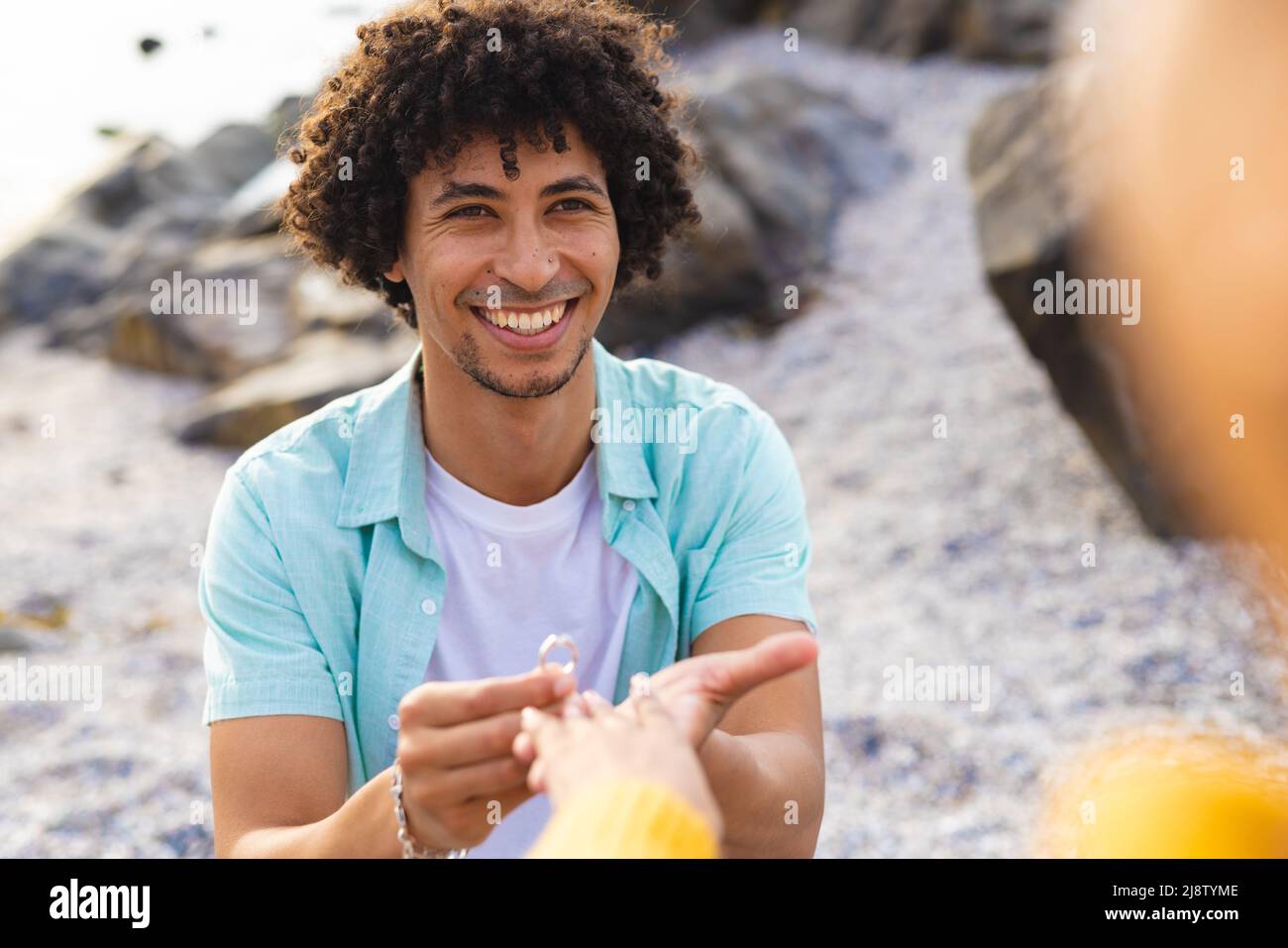 Allegro afroamericano uomo mettere anello di fidanzamento nel dito della ragazza alla spiaggia Foto Stock
