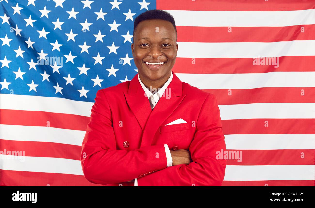 Felice bell'uomo afroamericano in abito rosso in piedi contro la bandiera degli Stati Uniti sfondo Foto Stock