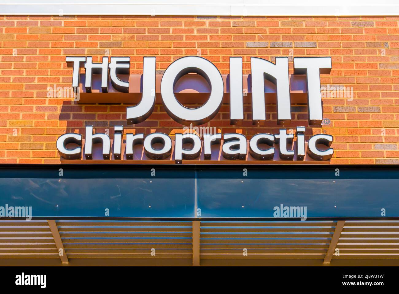Facciata esterna marchio e logo segnaletica per 'The Joint' Chiropractic struttura sanitaria in lettere bianche in una luminosa giornata di sole. Foto Stock
