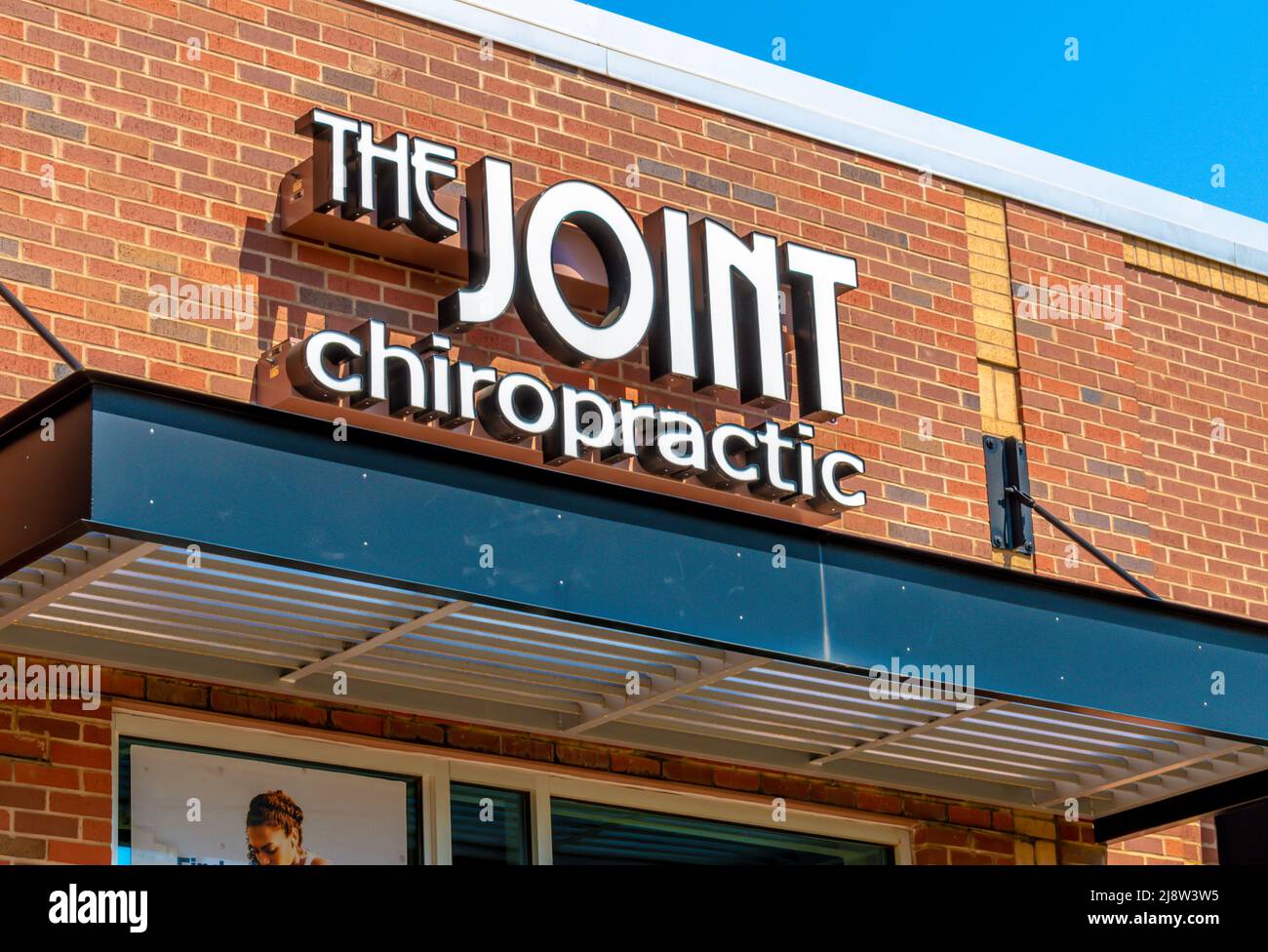 Facciata esterna marchio e logo segnaletica per 'The Joint' Chiropractic struttura sanitaria in lettere bianche in una luminosa giornata di sole. Foto Stock
