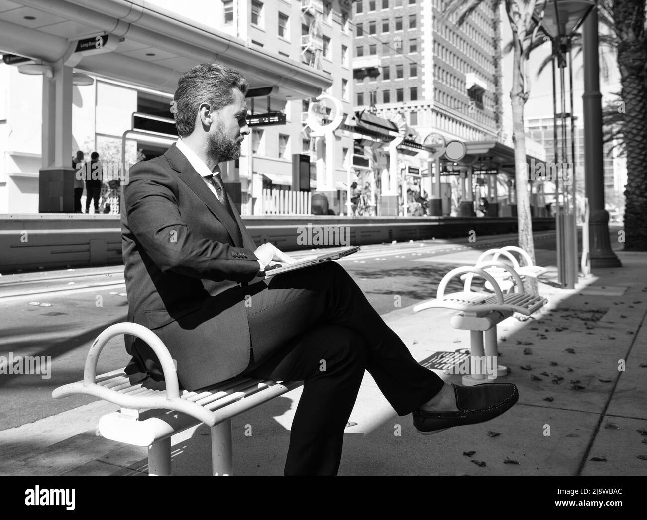 uomo maturo uomo d'affari in tuta siediti su panca in città all'aperto andando a lavorare on-line su laptop, business Foto Stock