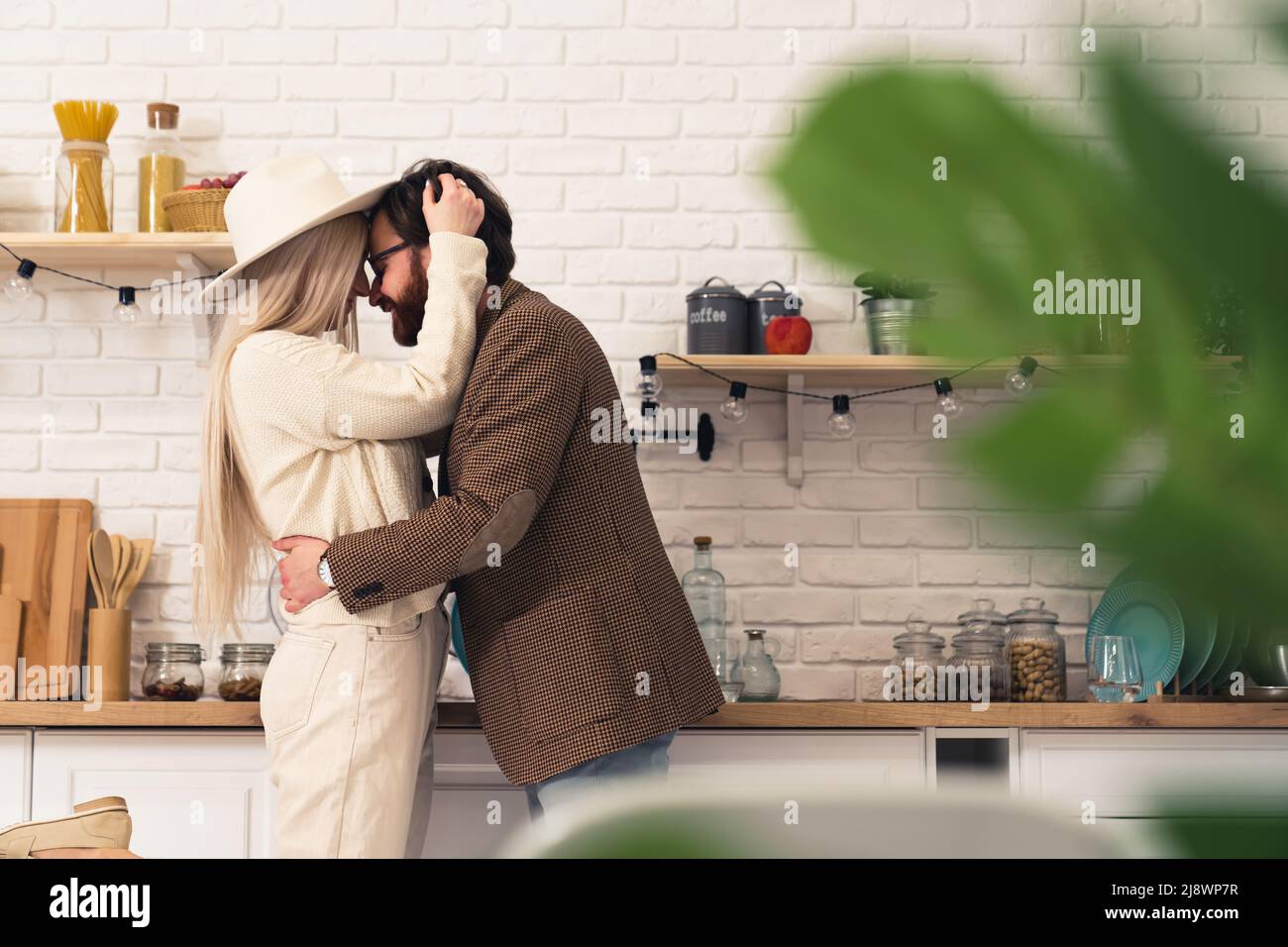 Bell'uomo bearded dai capelli scuri che abbraccia una donna caucasica bionda in piedi in un interno moderno della cucina. Foto di alta qualità Foto Stock