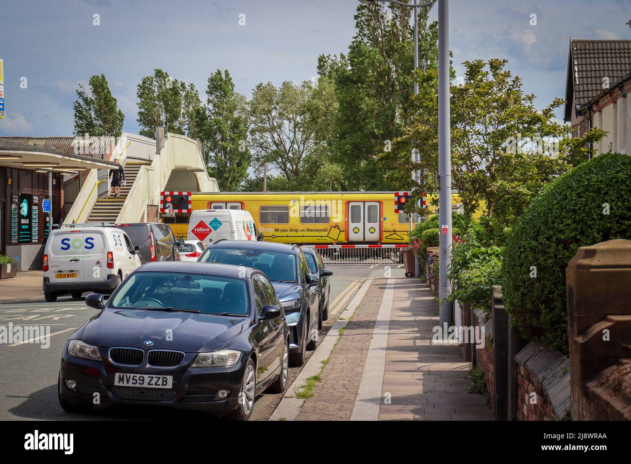 Hoylake stazione ferroviaria, barriere giù con il treno che passa attraverso la stazione Foto Stock
