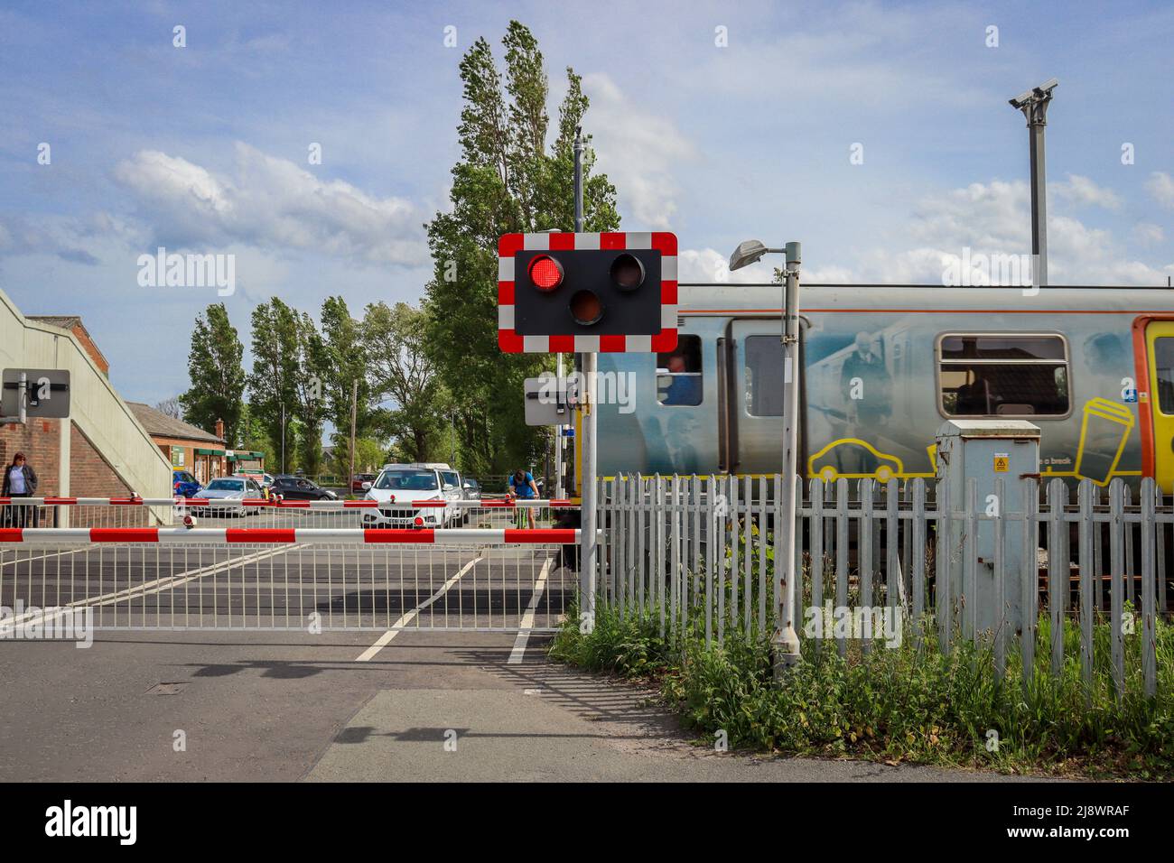 Hoylake stazione ferroviaria, barriere giù con il treno che passa attraverso la stazione Foto Stock