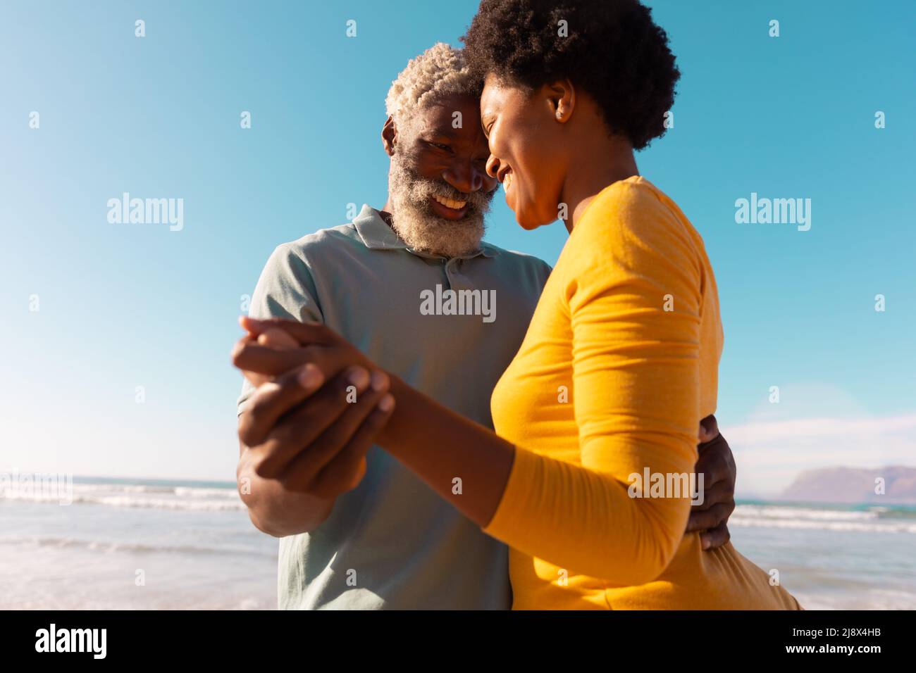Felice coppia romantica afroamericana danzare in spiaggia contro il cielo blu chiaro in giorno di sole Foto Stock