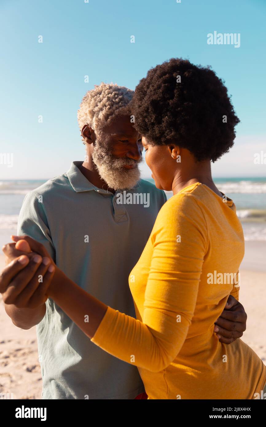 Romantica coppia afroamericana che balla in spiaggia contro il mare e il cielo blu chiaro in giorno di sole Foto Stock