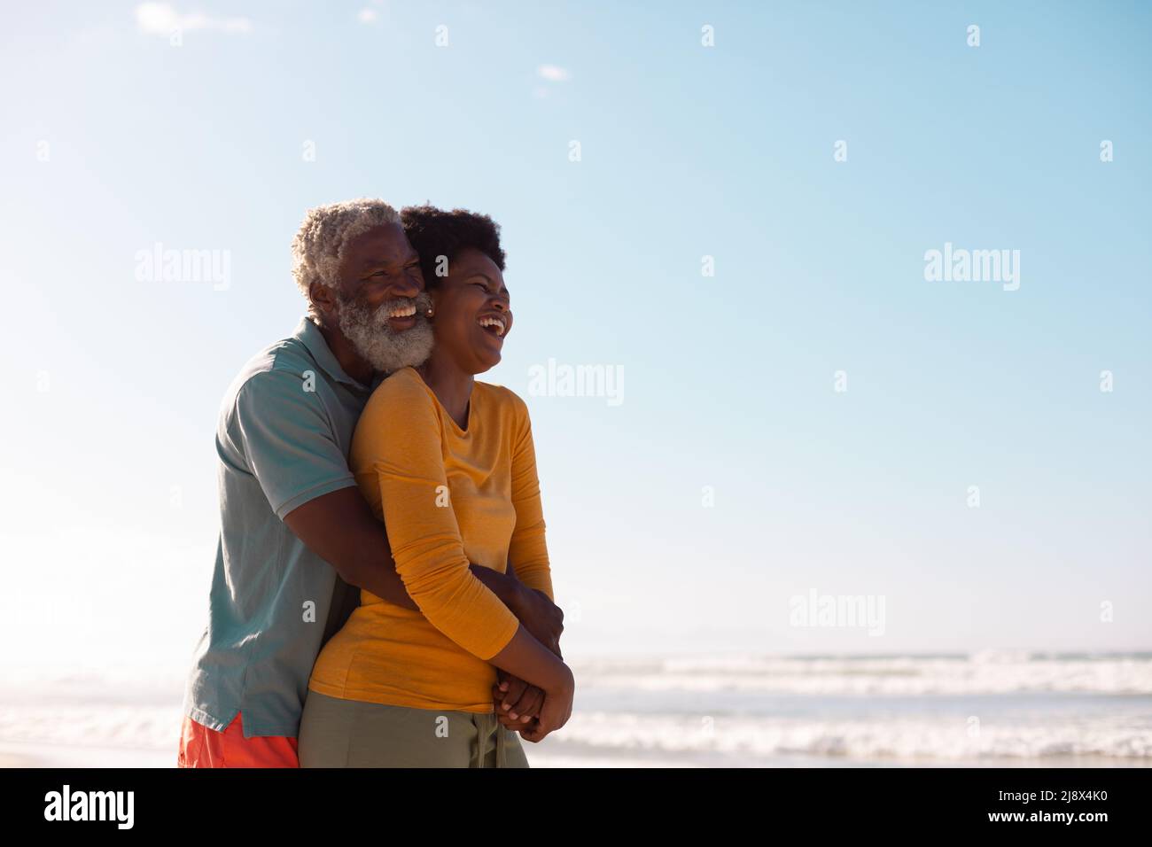 Allegro uomo anziano afroamericano che abbraccia la donna matura contro il mare e il cielo blu Foto Stock