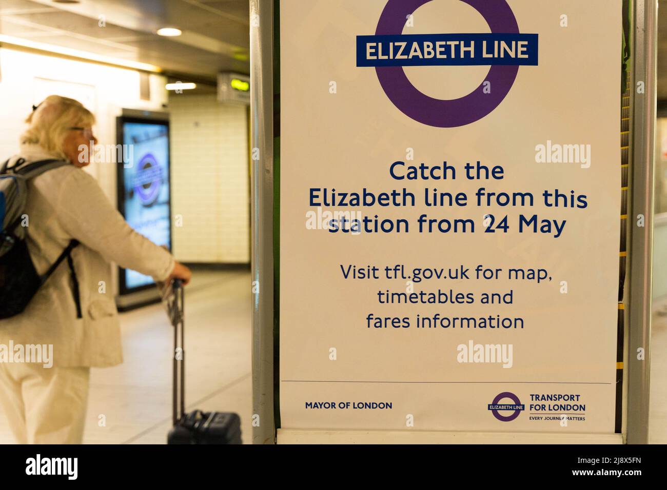 La donna guarda un poster che informa i passeggeri che 'prendere la linea Elizabeth da questa stazione dal 24 maggio' alla stazione metropolitana di Londra Inghilterra Regno Unito Foto Stock