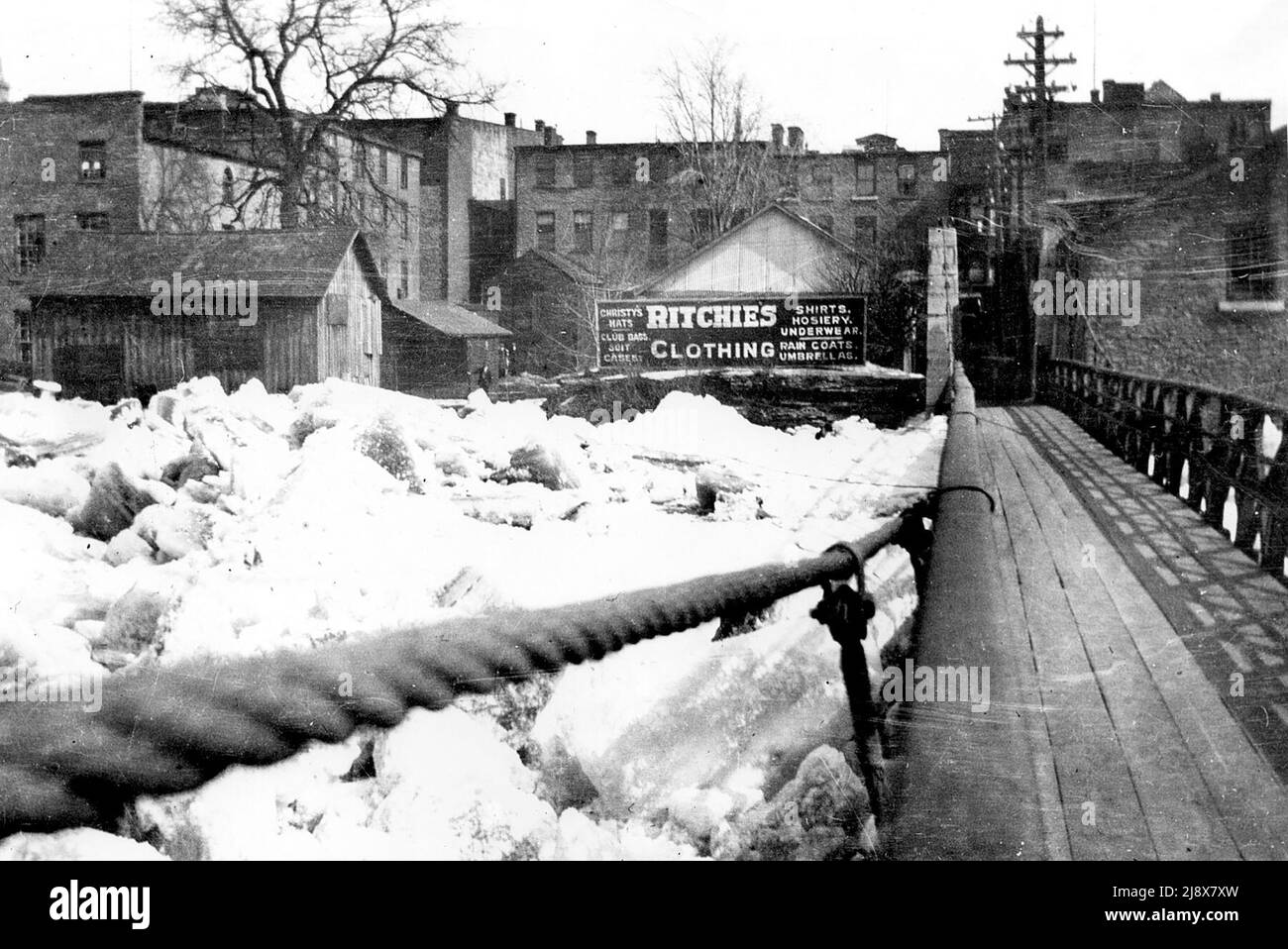 Ammira la passerella a Belleville, Ontario, guardando a est verso Front Street, mostrando la pubblicità per il negozio di abbigliamento Ritchie's. La marmellata di ghiaccio è alta contro la passerella ca. 1914 Foto Stock