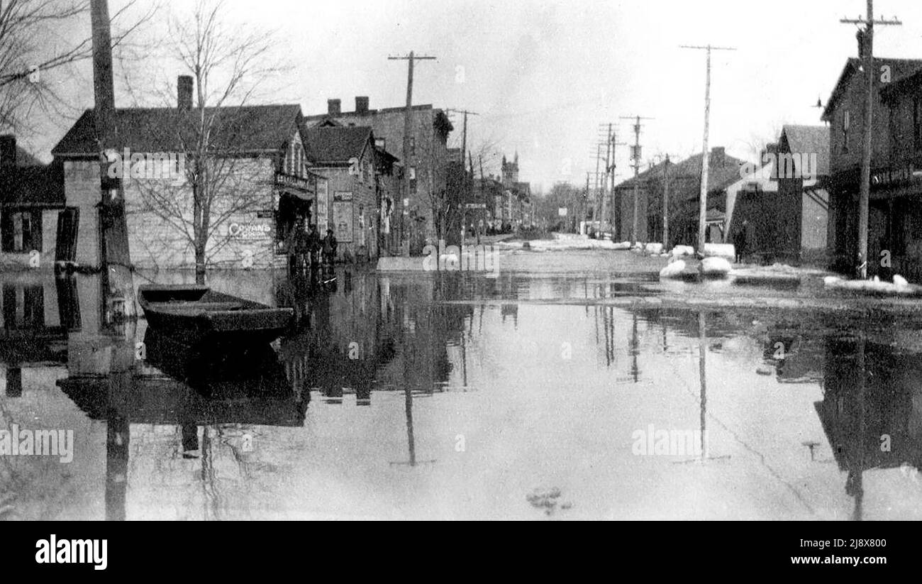 Una barca legata a un lampione su Bridge Street West, vicino a Everett Street a Belleville, Ontario, durante le inondazioni del 1918. Il negozio Kellaway General è sulla sinistra. La torre della Chiesa Metodista di Bridge Street è sullo sfondo ca. 1918 Foto Stock