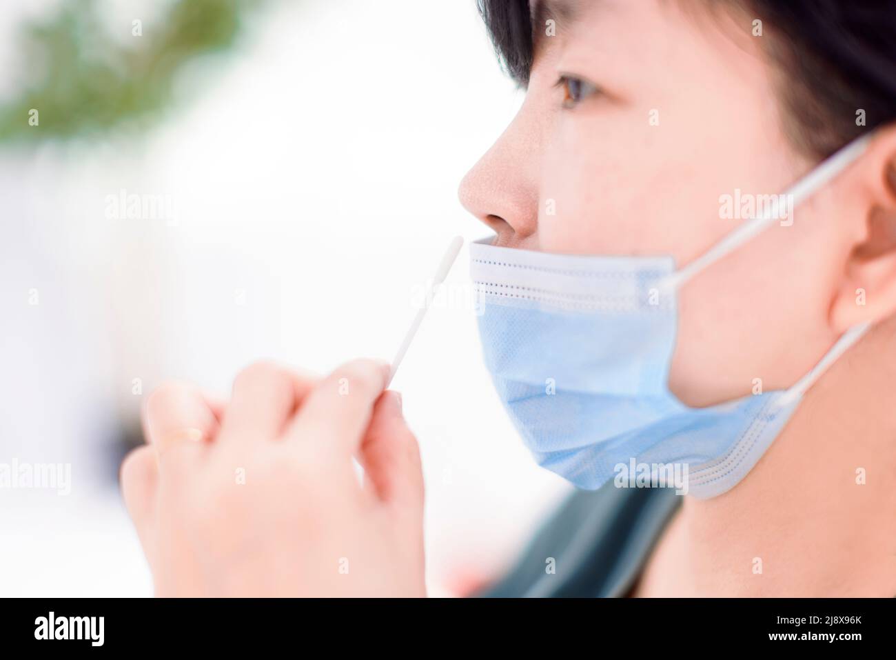 Donna che usa il kit auto-test dell'antigene rapido covid-19 a casa con un tampone nasale di cotone Foto Stock