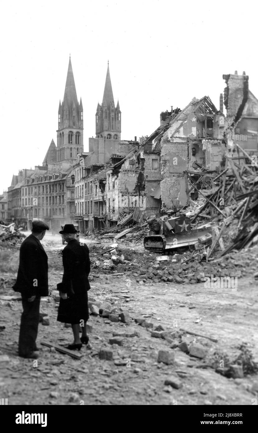 Un paio di residenti guarda un bulldozer canadese che cancella le rovine di case distrutte, rue de Bayeux, Caen. Sullo sfondo, le due torri dell'Abbaye aux Hommes rimangono intatte ca. 1944 Foto Stock