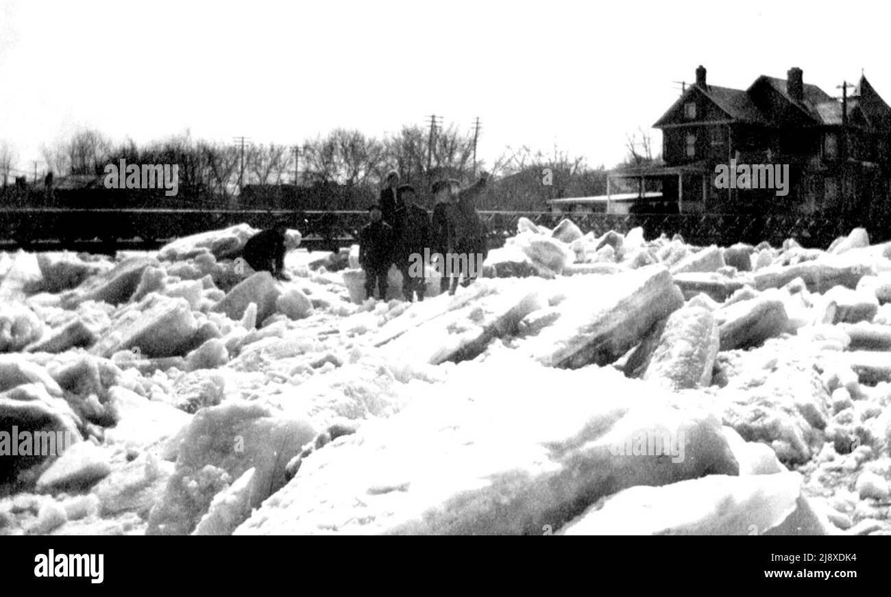 Persone in piedi su blocchi di ghiaccio accanto al ponte pedonale sul fiume Moira a Belleville, Ontario, durante l'alluvione 1918. La casa sulla destra è 1 Catharine Street ca. 1918 Foto Stock