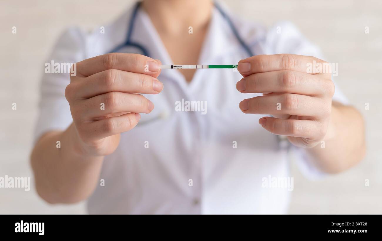 Il medico mantiene un test di gravidanza positivo. Il ginecologo senza volto raccomanda l'uso di test di gravidanza rapida. Foto Stock