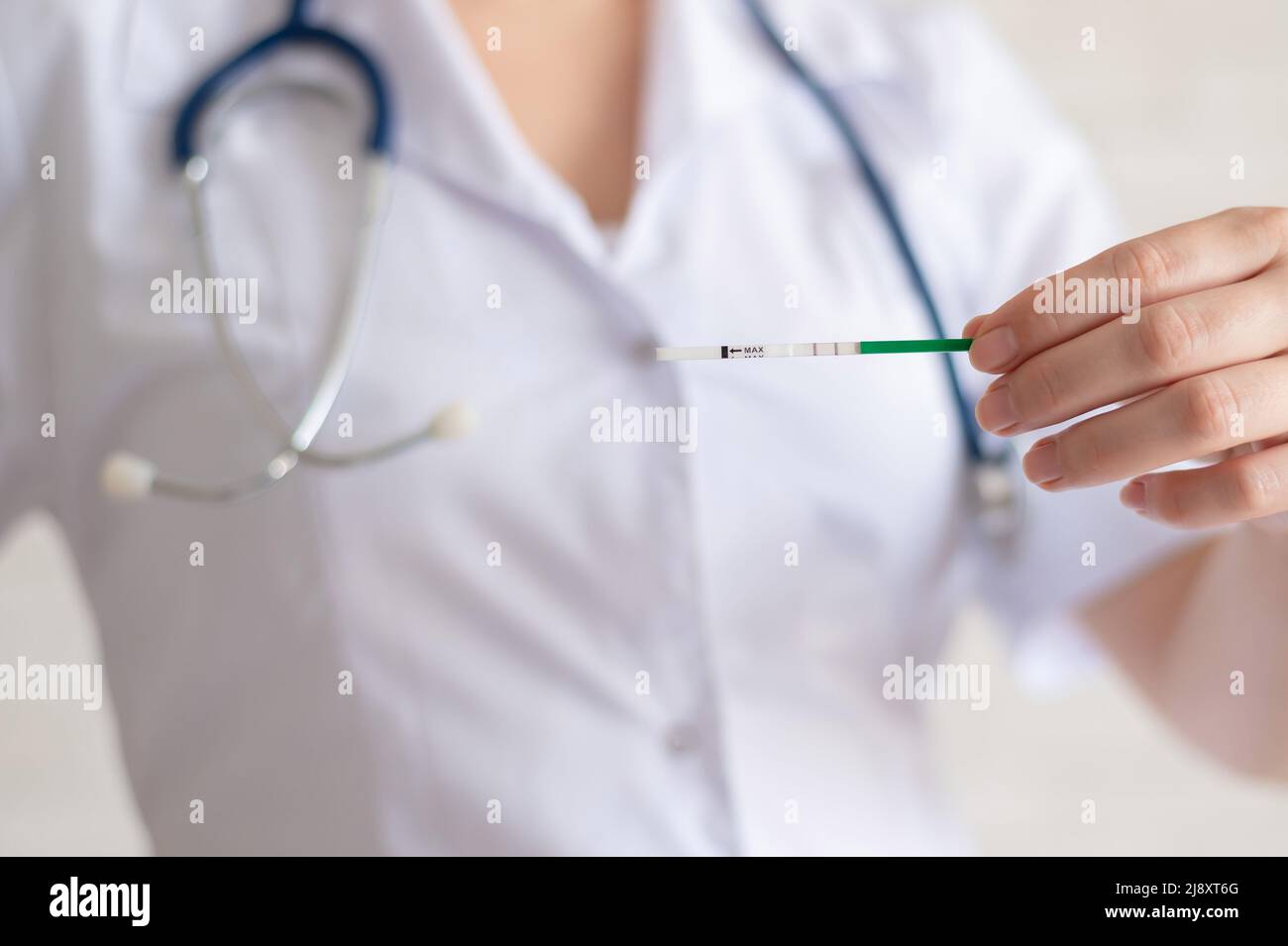 Il medico mantiene un test di gravidanza positivo. Il ginecologo senza volto raccomanda l'uso di test di gravidanza rapida. Foto Stock