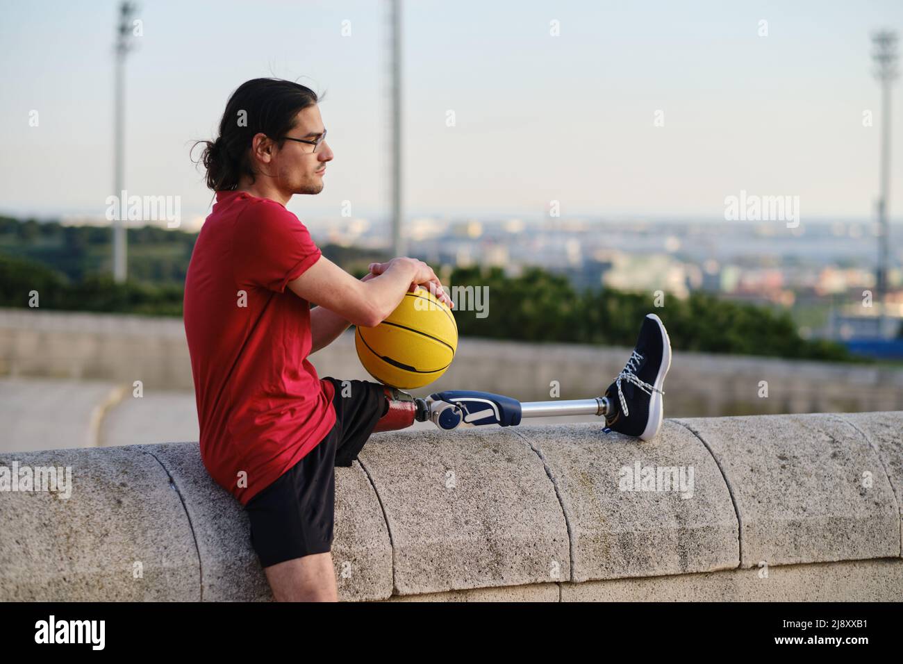 Giovane con disabilità che tiene una pallacanestro mentre si rilassa all'aperto dopo l'allenamento. Foto Stock