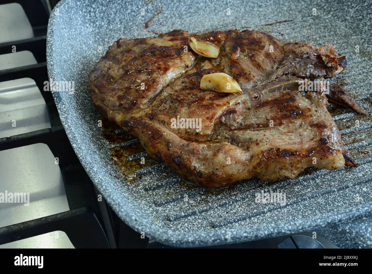 Pezzo di carne fritta con aglio in padella. Bistecca di carne alla griglia con aglio. Carne di maiale ben fatta Foto Stock
