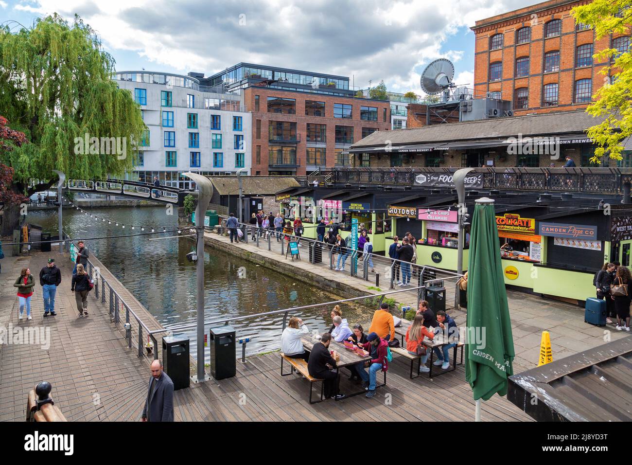 La gente si siede per mangiare all'aperto, in mezzo alla pletora di venditori di cibo al famoso West Yard a Camden Market, Londra, Regno Unito. Foto Stock