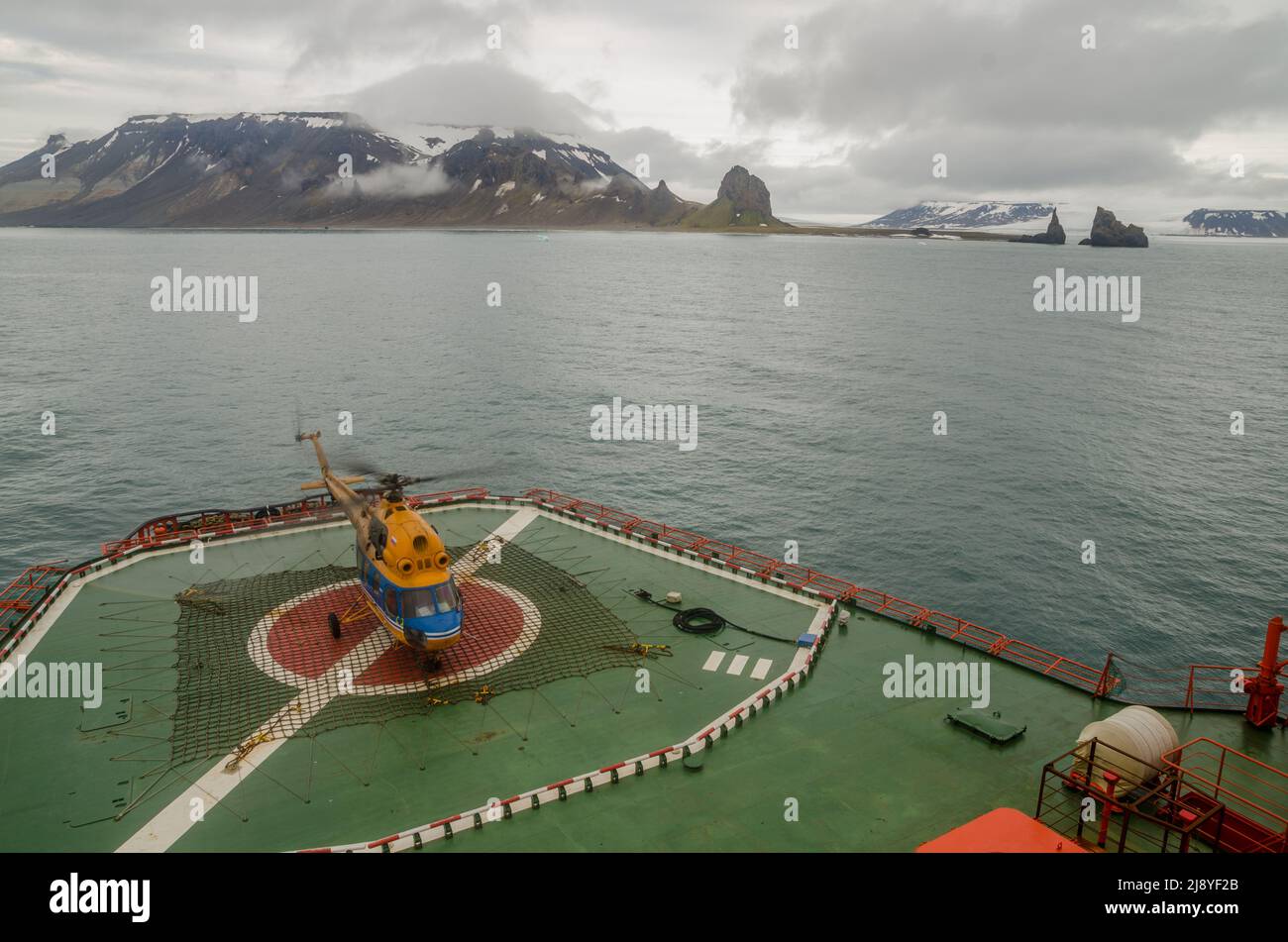 Un elicottero sul retro dei 50 anni di Vittoria (50 Let Pobody) rompighiaccio nucleare con Capo Tegethoff, Hall Island, Franz Josef Land, dietro Foto Stock