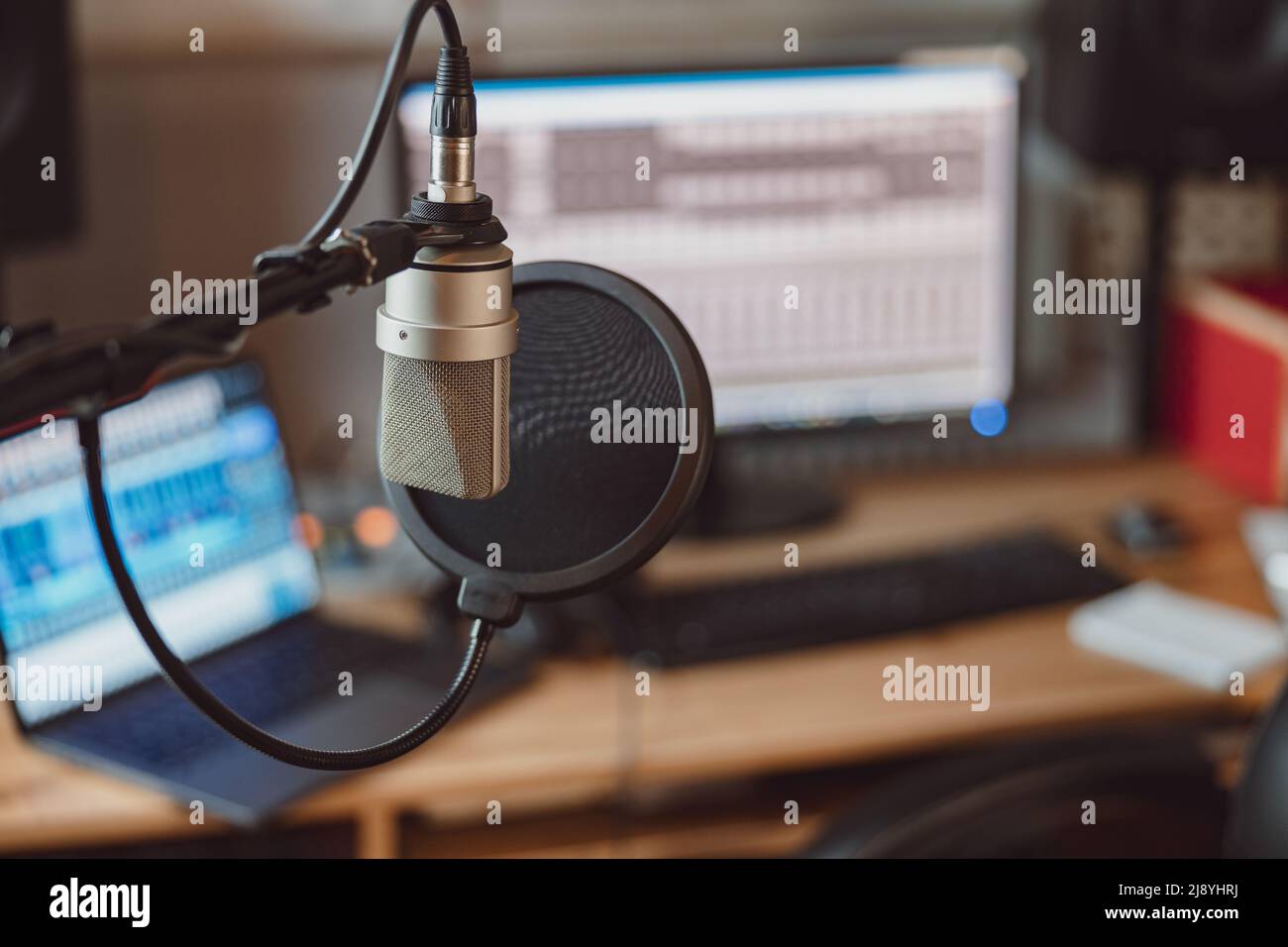 Messa a fuoco morbida su un microfono professionale sullo sfondo sfocato del notebook e dello schermo dello studio di registrazione del suono Foto Stock