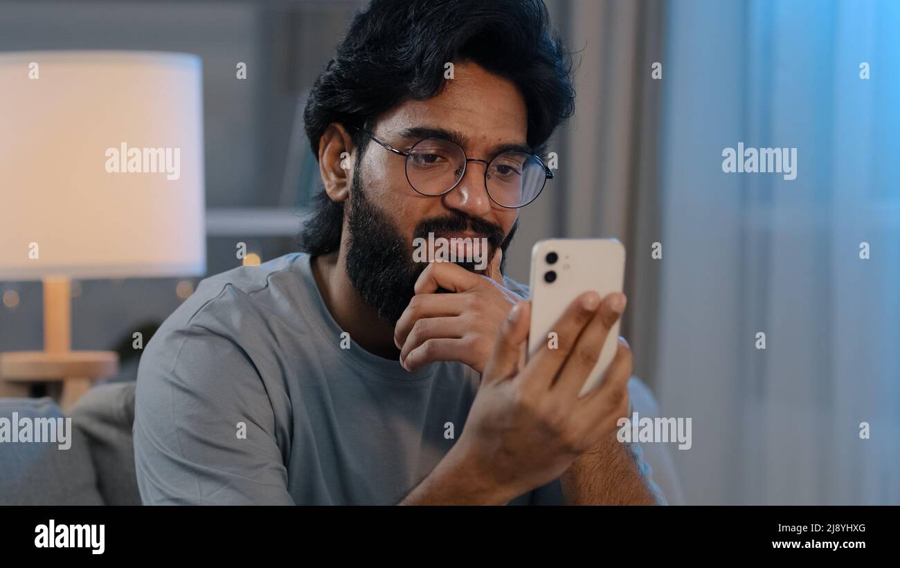 Arabo 30s uomo in occhiali a casa con telefono cellulare parlare in videochiamata conferenza chat distanza parlare utilizzando smartphone per casuale virtuale Foto Stock