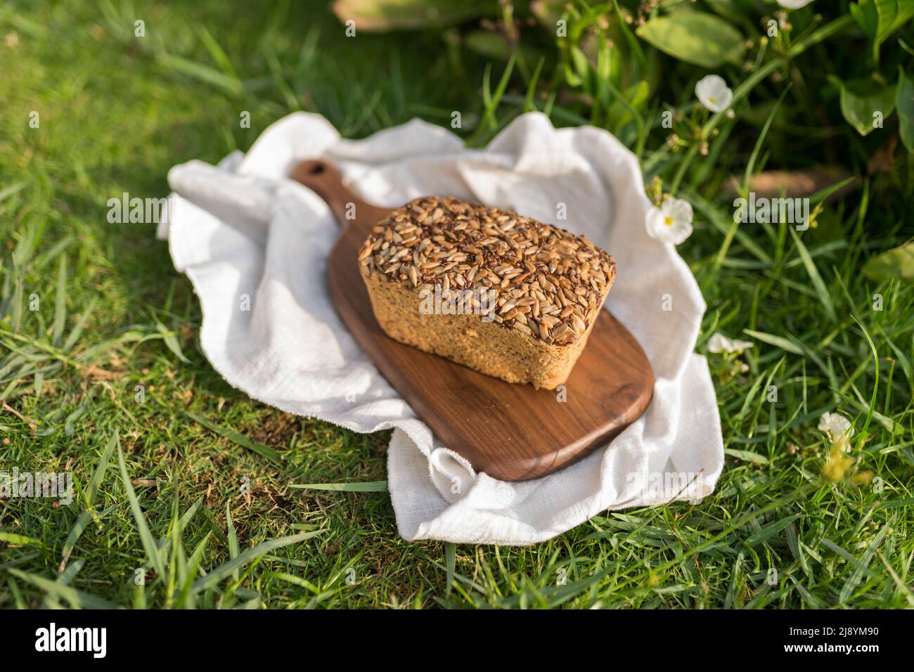 pane grigio fatto in casa con i semi sul bordo di legno con il tovagliolo di panno bianco sull'erba verde. Foto di alta qualità Foto Stock