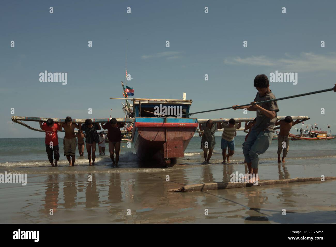 Uomini che spingono e tirano una barca da pesca con una corda sulla spiaggia di Malabero (Malabro) in Bengkulu, Indonesia. Foto Stock