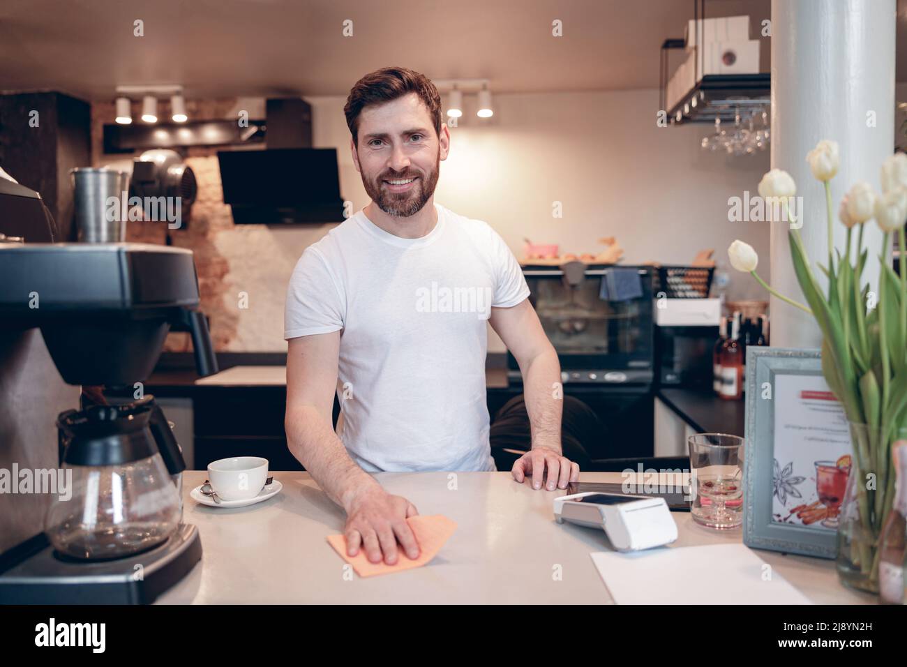 Bel caucasico felice uomo barista banco pulizia e sorridente alla macchina fotografica. Lavoro in caffetteria. Foto Stock