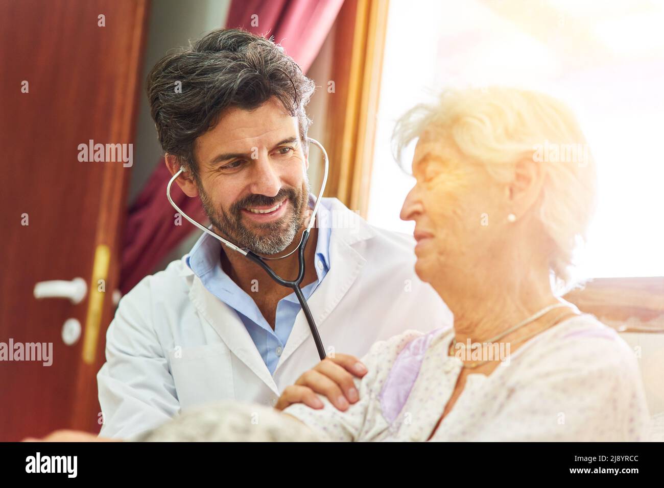 Il medico ascolta il paziente anziano con stetoscopio durante l'esame della visita domiciliare a letto Foto Stock
