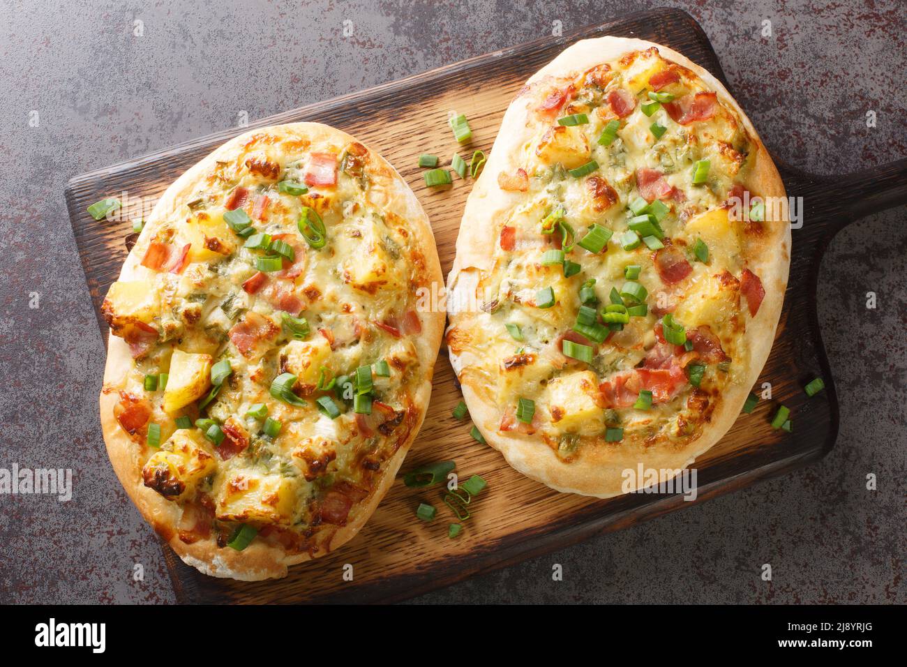 Pizza tedesca tradizionale con formaggio, patate, cipolle e pancetta da vicino su un asse di legno sul tavolo. Vista dall'alto orizzontale Foto Stock