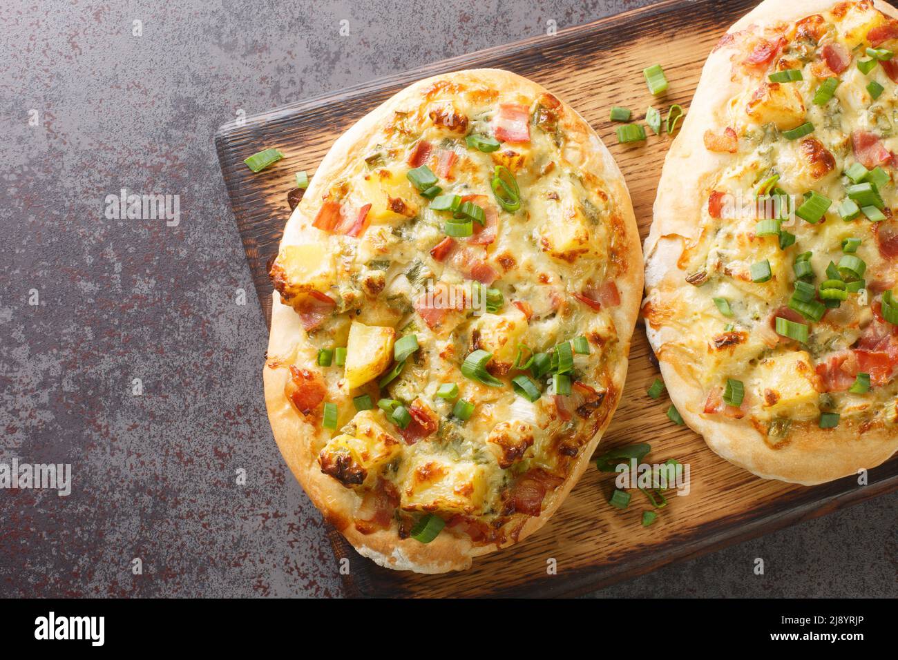 Torta aperta con formaggio, patate, cipolle e pancetta da vicino su un asse di legno sul tavolo. Vista orizzontale dall'alto Foto Stock